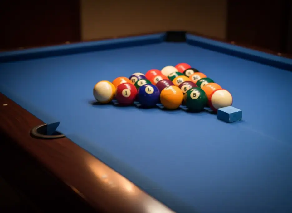 A racked set of pool balls on blue cloth with a chalk cube on the rail